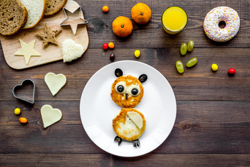 Funny breakfast for children. Meal with cheesecake in shape of owl. Dark wooden background top view