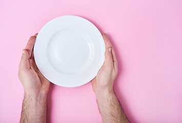 Empty ceramic round plate in man's hands isolated on pink background