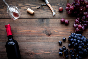 Open wine bottle. Grape and corkscrew on dark wooden background top view copyspace