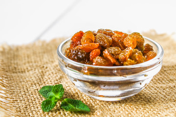 Golden Raisins from dried grapes in a glass bowl on sacking on a white wooden table of boards. Ingredients for cooking.