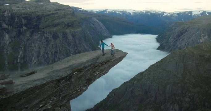 Couple Man and Woman on Trolltunga cliff mountains Love and Travel emotions Lifestyle concept. Young family traveling together active adventure vacations in Norway