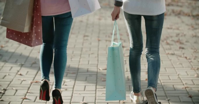 close-up of two Asian girls attractive girls with shopping bags walking down the street and looking at camera with smile