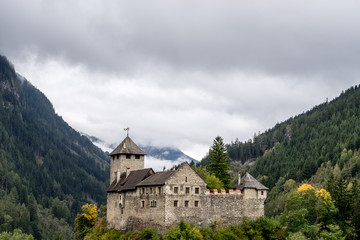Fototapeta na wymiar Schloss Wiesberg Castle with bridge over the Trisanna river. Mountain, colored hills and trees landscape natural environment on background. Paznautal Valley, Paznaun, Tyrol, Austria.