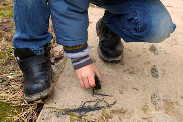 a child draws with charcoal on the pavement