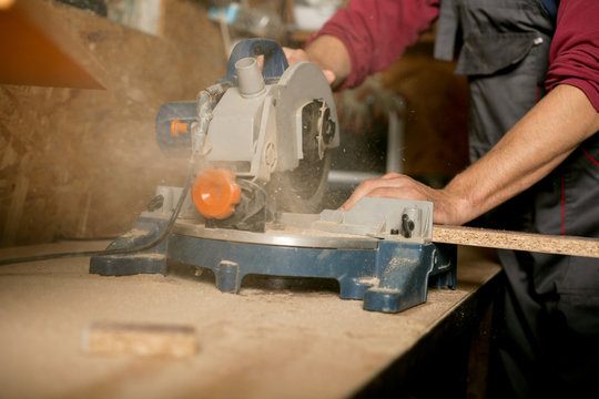 Skilled carpenter cutting a piece of wood in his woodwork workshop, using a circular saw