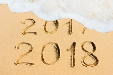  New Year concept - 2017 and 2018 handwritten in the sandy beach with soft ocean wave
