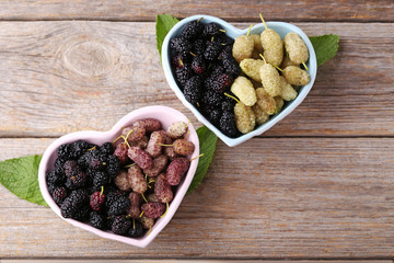 White, black and purple mulberries in bowls on wooden table