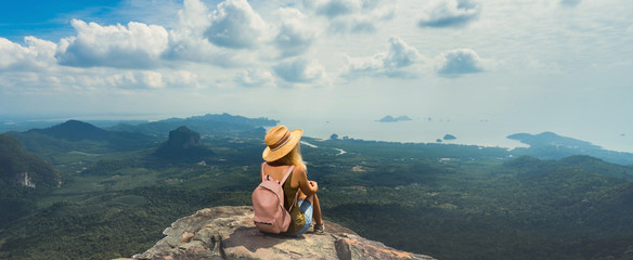 Young woman with backpack enjoying breathtaking view of the landscape from the top of mountain....