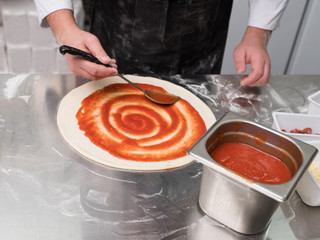 Chef spreading pizza tomato sauce on a dough following a traditional italian recipe. Cooking delicious food at restaurant every day