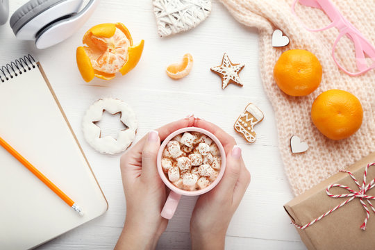 Female hands holding cup of coffee with marshmallow, gingerbread cookies and mandarin
