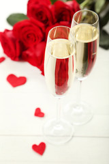 Champagne glasses with bouquet of red roses on wooden table