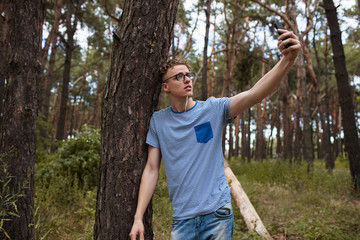 Naklejka na ściany i meble Self-confident man does selfie by the phone in the forest. Alone on the nature. Traveler lifestyle.