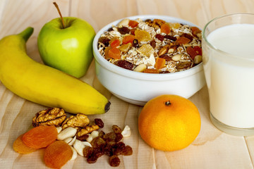 Healthy eating. On the wooden board are muesli, honey in a jar, a banana, an orange, a green apple,...