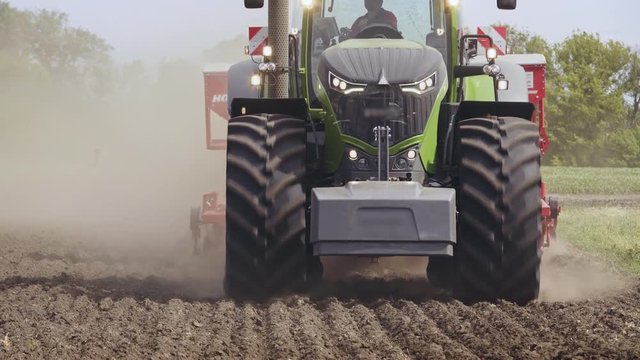 Agricultural tractor driving on arable field. Close up farming tractor moving with trailer seeder on plowed land. Process sowing farming field