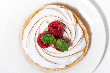 sweet tartlet with meringue and raspberry on white plate, top view
