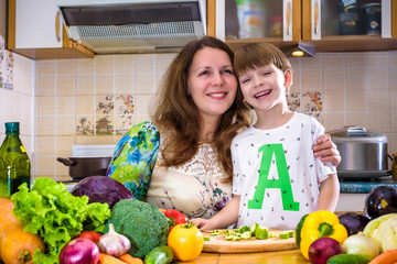 The young cook mother standing with her little son in the kitchen and salting vegetables