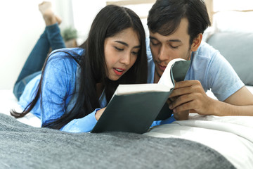 Young asian lover lying on the bed reading book in bedroom. concept of education, tutorial and learning.