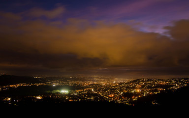 View of Bath at night from Solsbury Hill. The UNESCO World Heritage city seen nestling among hills from a high viewpoint, under low clouds