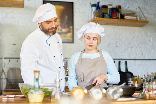 Portrait of smiling mature chef teaching female apprentice cooking in kitchen of modern restaurant