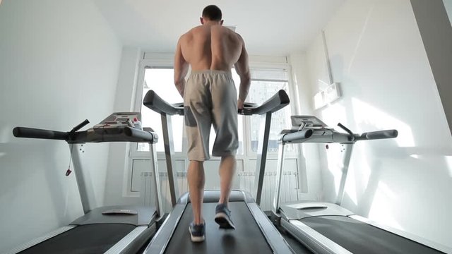 Man is walking along the treadmill, he has training in the gym.