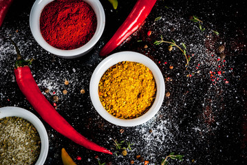 Various spices and seasonings. Cooking background.  Turmeric, curry, paprika, pepper, chili, dried basil, salt, fresh chili, thyme. Black rusty metal background. Top view, copy space.