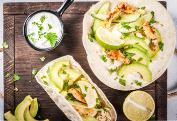 Healthy food snack. Tortillas taco with grilled chicken, avocado, fresh salsa, lettuce, lime. With yogurt & parsley sauce. On light gray stone marble table, wooden cutting board. Top view copy space