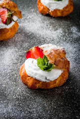 Summer desserts. Homemade baking. Cake profiteroles with whipped cream, fresh strawberries, mint and sprinkling of powdered sugar. On a black stone table. Copy space