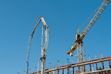 Ein Kran und eine Betonpumpe arbeiten an einem Neubau unter blauem Himmel