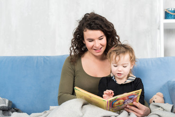 Young mother is reading a book to her cute daughter.