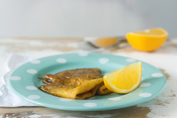 Crepe suzette in caramel sauce on a plate with a slice of orange. French dessert.