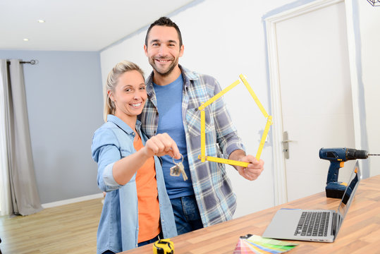 cheerful young couple making future project by renovating their new home and holding their house keys