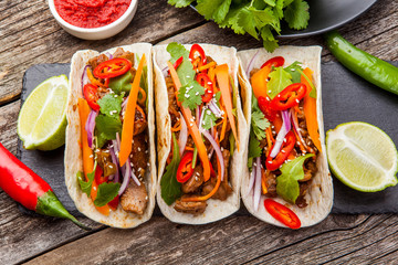 Three mexican tacos with meat and vegetables. Tacos al pastor on wooden dark background.