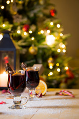 Two high glasses of christmas mulled wine with red apples, orange slices, cinnamon sticks and spices on wooden table with bokeh background. Selective focus.