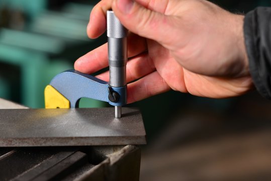Elderly worker looks in the drawing to see detail sizes. The man turner measures the dimensions of the part on a micrometer, and also uses a sliding caliper.