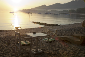 Fototapeta na wymiar Bali. A table and chairs on the beach by the sea in a northern part of the island at sunset..