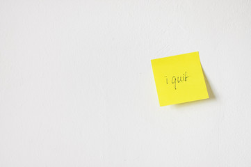 Neon yellow sticky note or post it with handwritten message saying 'I quit' on white textured office wall most likely about quitting smoking or giving notice from a job as new year's resolution