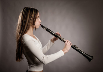 young woman playing a clarinet on a gray background