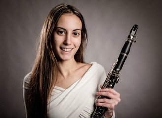 young woman holding a clarinet on a gray background