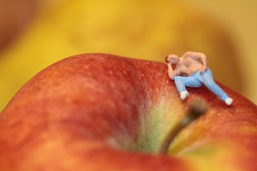 uomo in miniatura seduto su una mela rossa