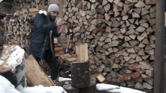 man splitting frozen wood with axe. wide shot slow motion