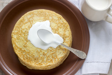 Stack of Russian pancakes with sour cream - blini on a plate on wooden table.