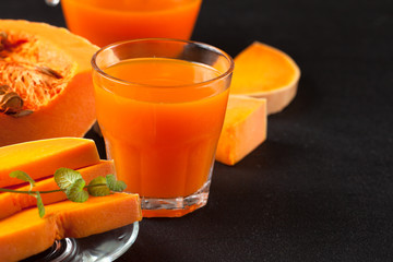 Pumpkin fresh juice in beautiful glasses and jug with pieces of ripe vegetable on brown wooden background. Sweet orange juice. Healthy eating, diet theme. Close up photography. Horizontal banner