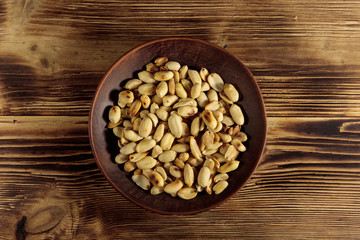 Roasted salted peanuts in plate on wooden table