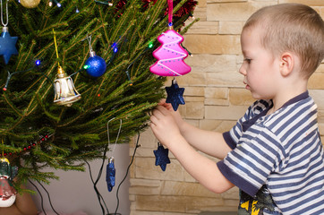 Dziecko wiesza ozdoby na choince bożonarodzeniowej. Widać chłopca i kolorowe lampki i ozdoby. © Rajtar photography