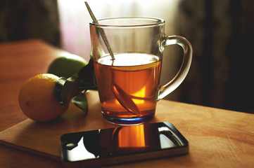 smartphone with cup of tea and lemon on wooden board