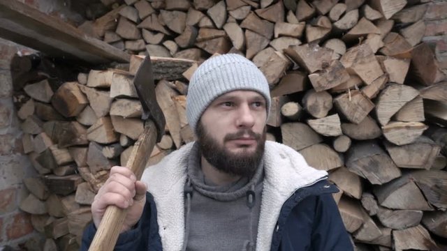 A man is a woodcutter with an ax against the background of a pile of firewood