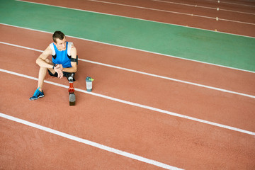High angle portrait of young amputee athlete sitting on running track taking break from practice  to relax, copy space