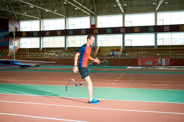 Obraz premium Side view portrait of amputee athlete running on track of indoor stadium preparing for Paralympic championship, copy space