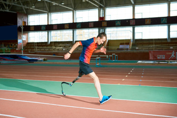 Obraz premium Full length portrait of amputee athlete running on track of indoor stadium preparing for Paralympic championship, copy space