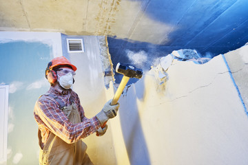 worker with sledgehammer at indoor wall destroying